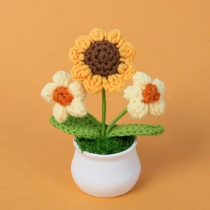 Detail van handgehaakte zonnebloem in witte pot met kleine witte accentbloemen