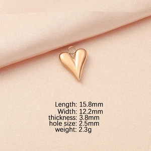 Golden heart-shaped pendant dimensions of 15.8mm by 12.2mm shown on pink fabric
