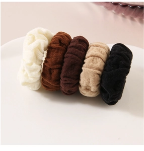 Close-up of five knitted ribbed hair scrunchies in neutral earth tones on a white plate