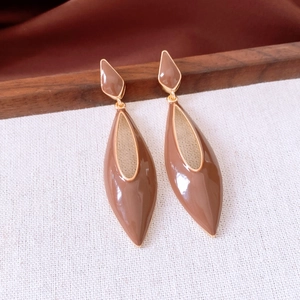 Gros plan de boucles d'oreilles goutte en émail marron et clous losanges dorés