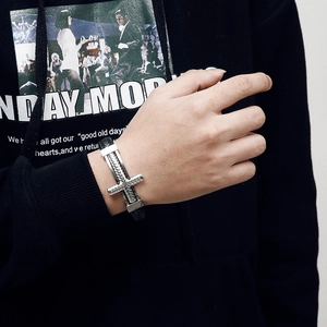 Close-up of a men's punk black braided leather bracelet featuring a silver cross charm
