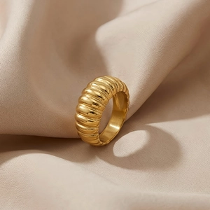 Detailed macro view of the polished golden ribbed stainless steel ring on pink silk fabric