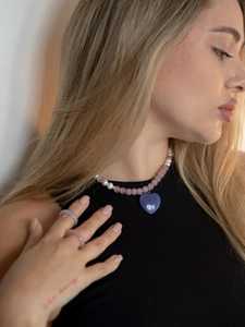 Detail of beaded necklace with blue heart pendant and round rings on model