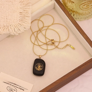 Close-up of gold snake chain with tree of life pendant on black stone on wooden tray