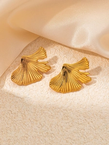 Detailed view of gold ginkgo leaf stud earrings with fine texture on silk fabric