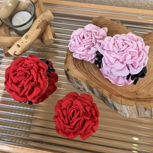 Detailed view of 3D fabric rose hair claws in red and pink on a rustic wooden display