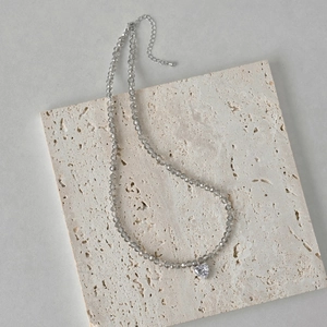 Close-up of S925 silver beaded necklace with crystal heart pendant on stone surface