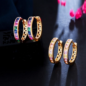 Golden hoop earrings with colorful zircon stones on a black background and pink flowers