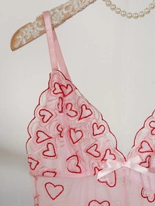 Détail de lingerie en dentelle rose avec broderie coeur rouge et nœud en ruban de soie