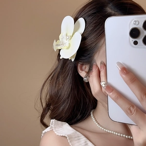 Close-up of realistic white orchid hair clip with faux pearl center on model
