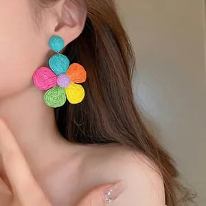 Handmade bohemian colorful woven raffia flower drop earrings worn by a model