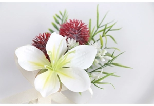 Close-up of artificial white lily boutonniere with red floral accents and green leaves