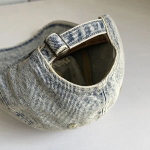 Detail view of washed blue denim baseball cap with adjustable metal buckle and strap