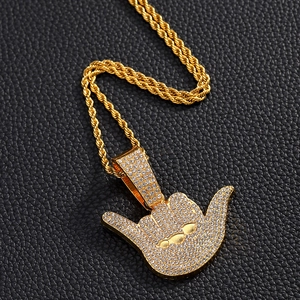 Macro detail of iced-out gold shaka hand pendant with thick rope chain on black leather