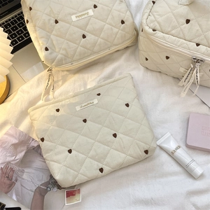 Three quilted heart makeup bags in cream with heart patterns and zipper closure on fabric