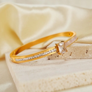 Gold stainless steel bangle with square zircon and mother of pearl on stone background