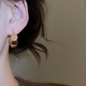 Close-up of gold hoop earrings featuring amber and clear square stones on model