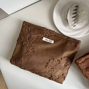 Detailed close-up of a camel suede cosmetic bag with exquisite floral embroidery and tag