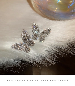 Macro detail of silver butterfly stud earrings with zircon stones on white plush background