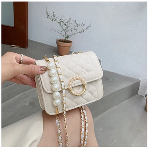 Detail of quilted crossbody bag with pearl strap and decorative round pearl clasp