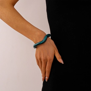 Detail of dark green wavy acrylic cuff bracelet worn by a model on black background