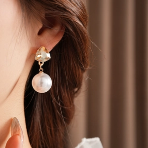 Close-up of elegant gold triangle stud earrings with a white pearl drop on model