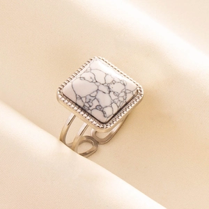 Macro shot of silver ring with square white marble stone on beige silk fabric