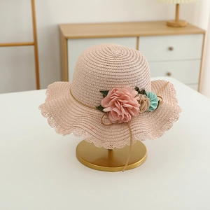Detail of a pink woven straw sun hat for girls with large fabric flowers and wavy brim