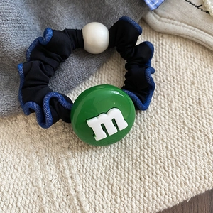 Gros plan détaillé d'un chouchou avec un pendentif m vert et une grosse perle crème