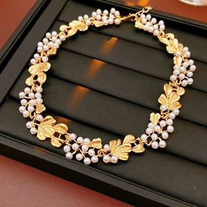 Detail view of a vintage gold leaf and pearl necklace on a black textured jewelry tray