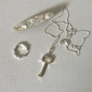 Flat lay of a 925 silver key necklace, wave ring, and marble acetate hair clip