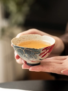 Detailed view of hand-painted blue and red ceramic tea cup held with golden line accents