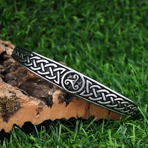 Detailed view of silver Celtic triskele knot bangle on natural cork and green moss background