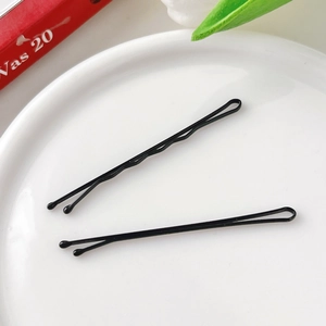 Macro detail of two black metal hair clips on a white ceramic plate with a natural backdrop