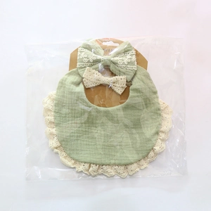 Detailed view of sage green muslin baby bib with beige lace trim and matching headband