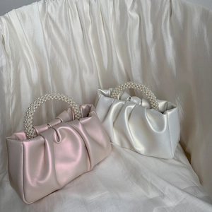Detail of pink and white pleated cloud bags featuring elegant pearl handles on soft fabric