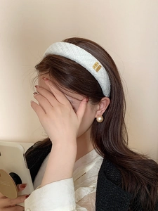 Dettaglio fascia per capelli in tweed imbottita con logo dorato e orecchino di perla