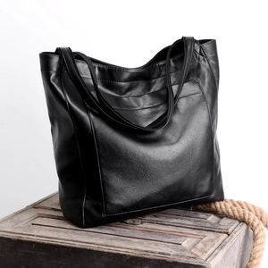 Détail d'un cabas vintage en cuir ciré noir posé sur un coffre en bois rustique