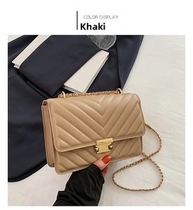 Detail of khaki chain bag featuring V-shaped quilted stitching and gold square metal lock