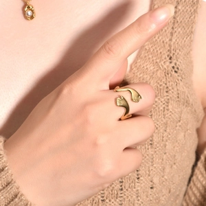 Detailed view of a gold hugging hands open ring paired with an elegant pearl necklace