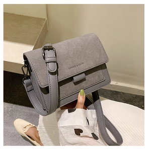 Detail shot of grey faux leather small square bag featuring metal strap buckle and logo