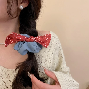 Detail view of sky blue fabric scrunchie with red white polka dot bow in a low braid ponytail