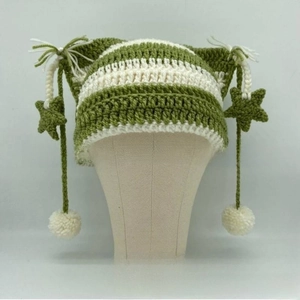 Detailed knit texture of a cat-ear beanie with green stars and fluffy white pompoms
