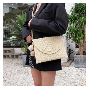Detail of straw woven envelope bag with decorative pom-poms and leather shoulder strap