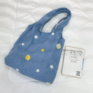 Detail of blue faux shearling tote bag with embroidered star and planet patterns