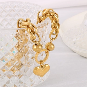 Detail shot of heart-shaped charm and thick gold chain link on a glass container
