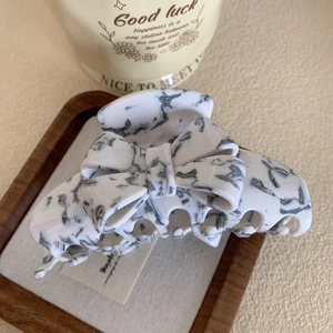 Détail d'une grande pince à cheveux en acétate avec texture marbre blanc et nœud