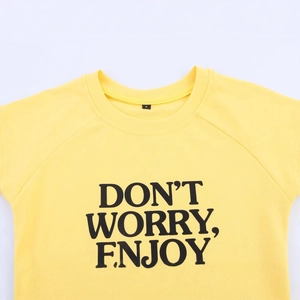 Camiseta amarilla de cuello redondo con eslogan negro Don't Worry Enjoy en fondo blanco