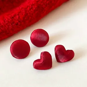 Eleganti orecchini a lobo in tessuto rosso tondi e a cuore con trama a saia su sfondo bianco