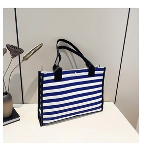 Detail of blue and white striped canvas tote bag with black leather handle and metal snap